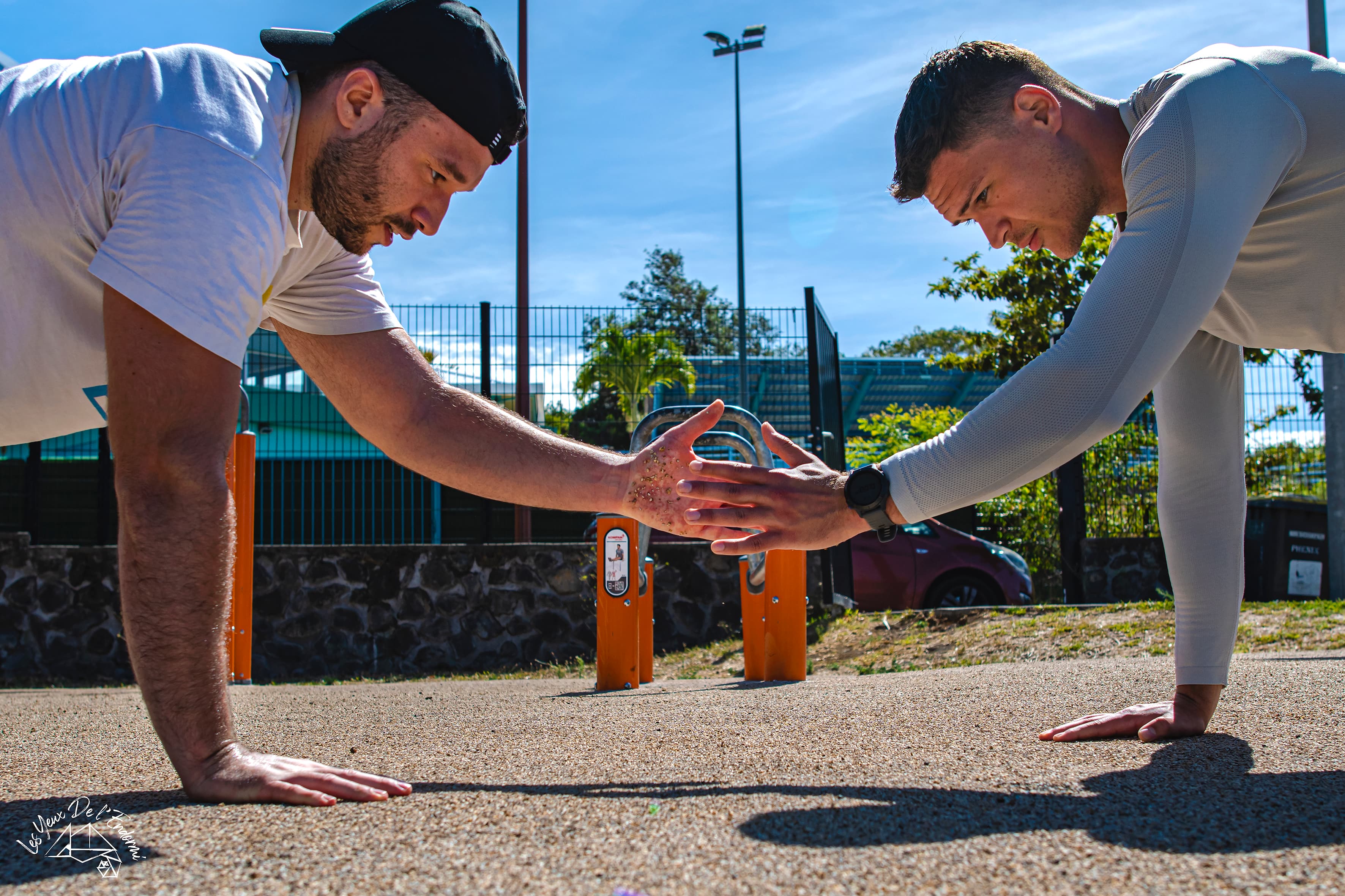 Ludovic et un client se tapent dans la main en position de pompe, sur une aire de street workout en extérieur.